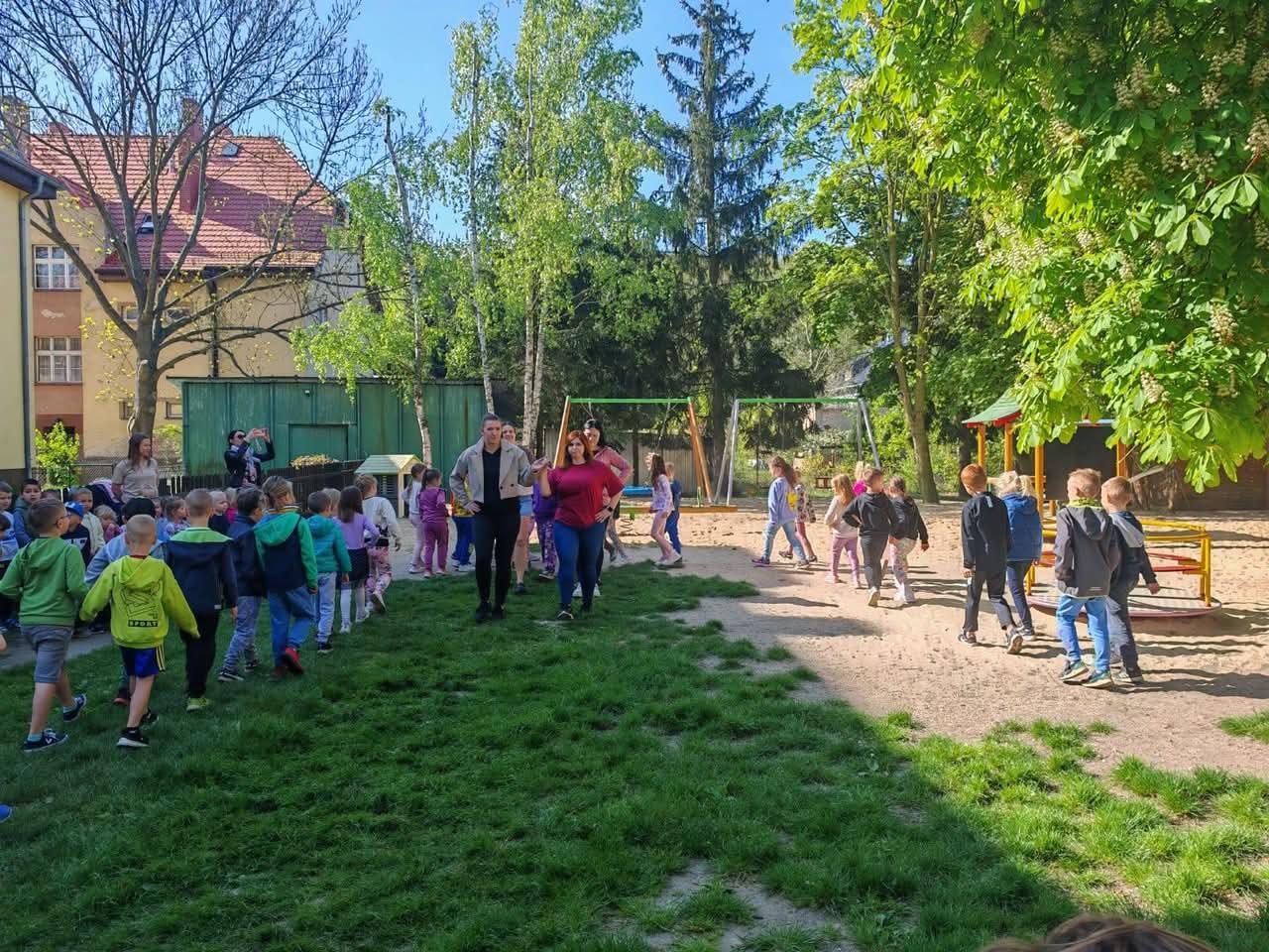 Nauczyciele wraz z dziećmi tańczący poloneza w ogrodzie przedszkolnym