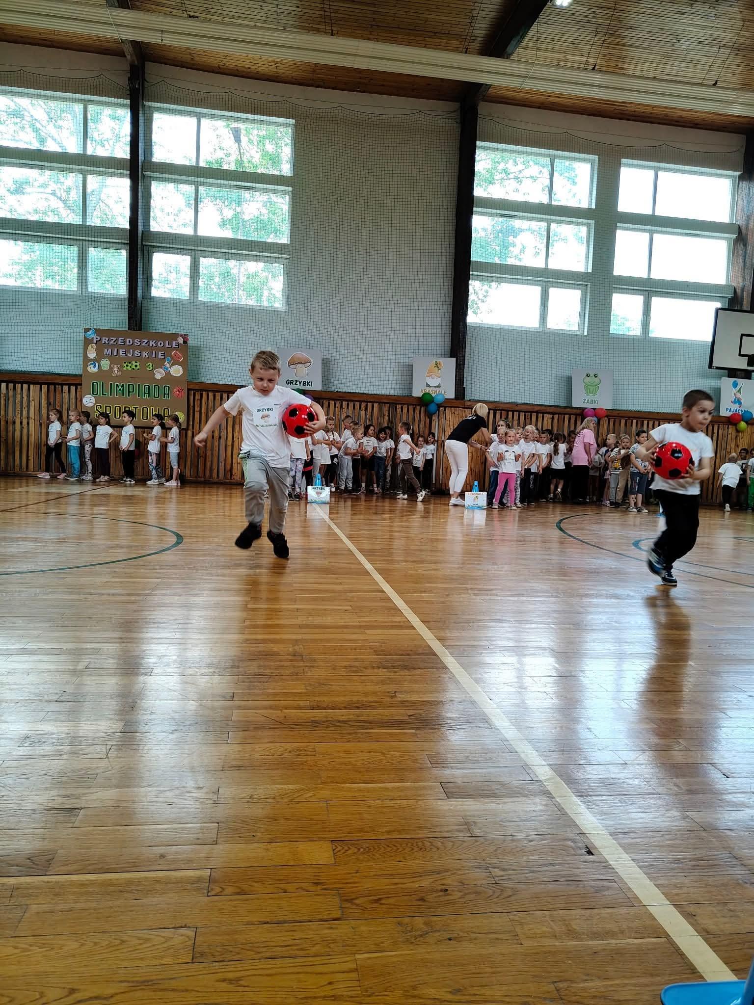 Dzieci biegnące z piłką na hali sportowej