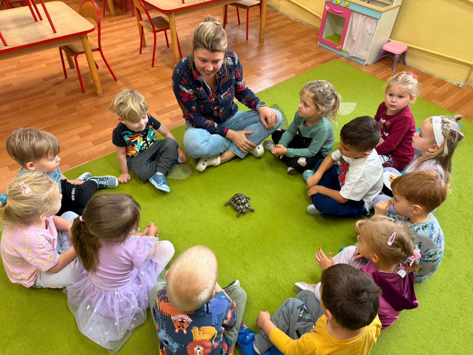 Dzieci z nauczycielem siedzą w kole na środku jest żółw