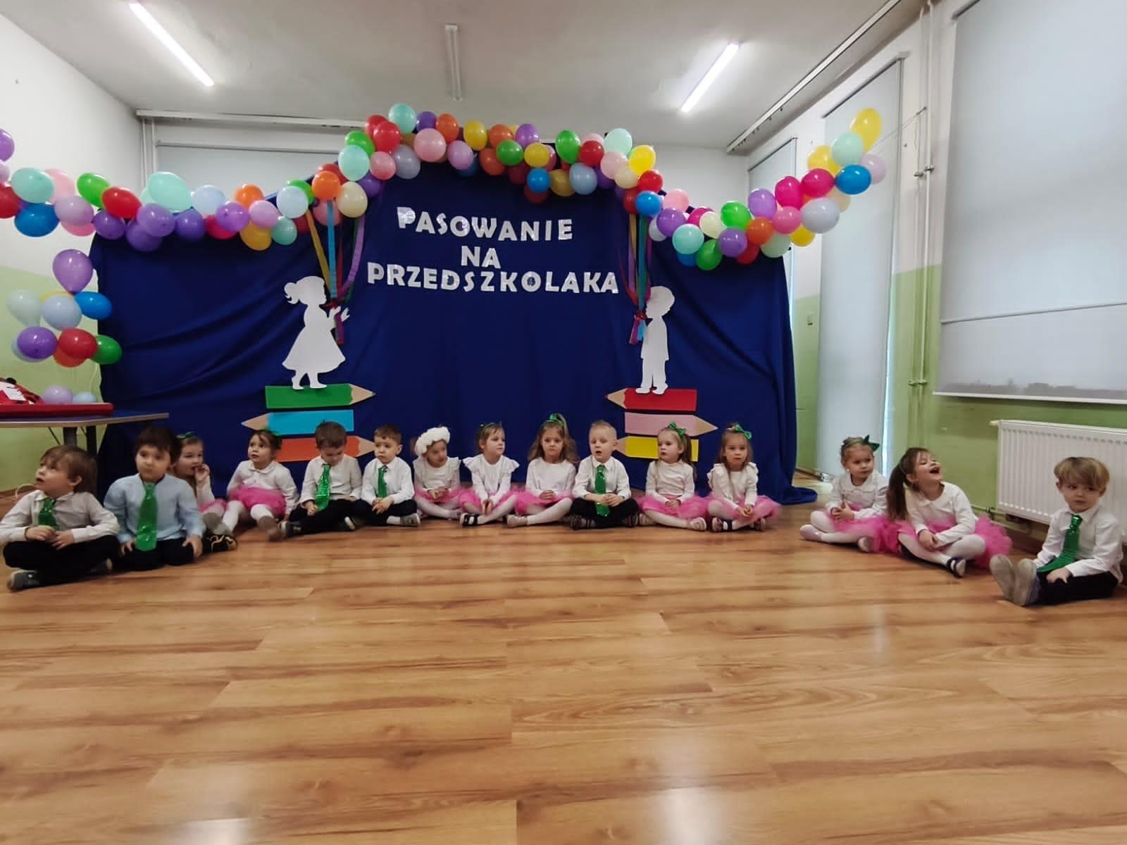 Dzieci siedzące w półkolu na sali