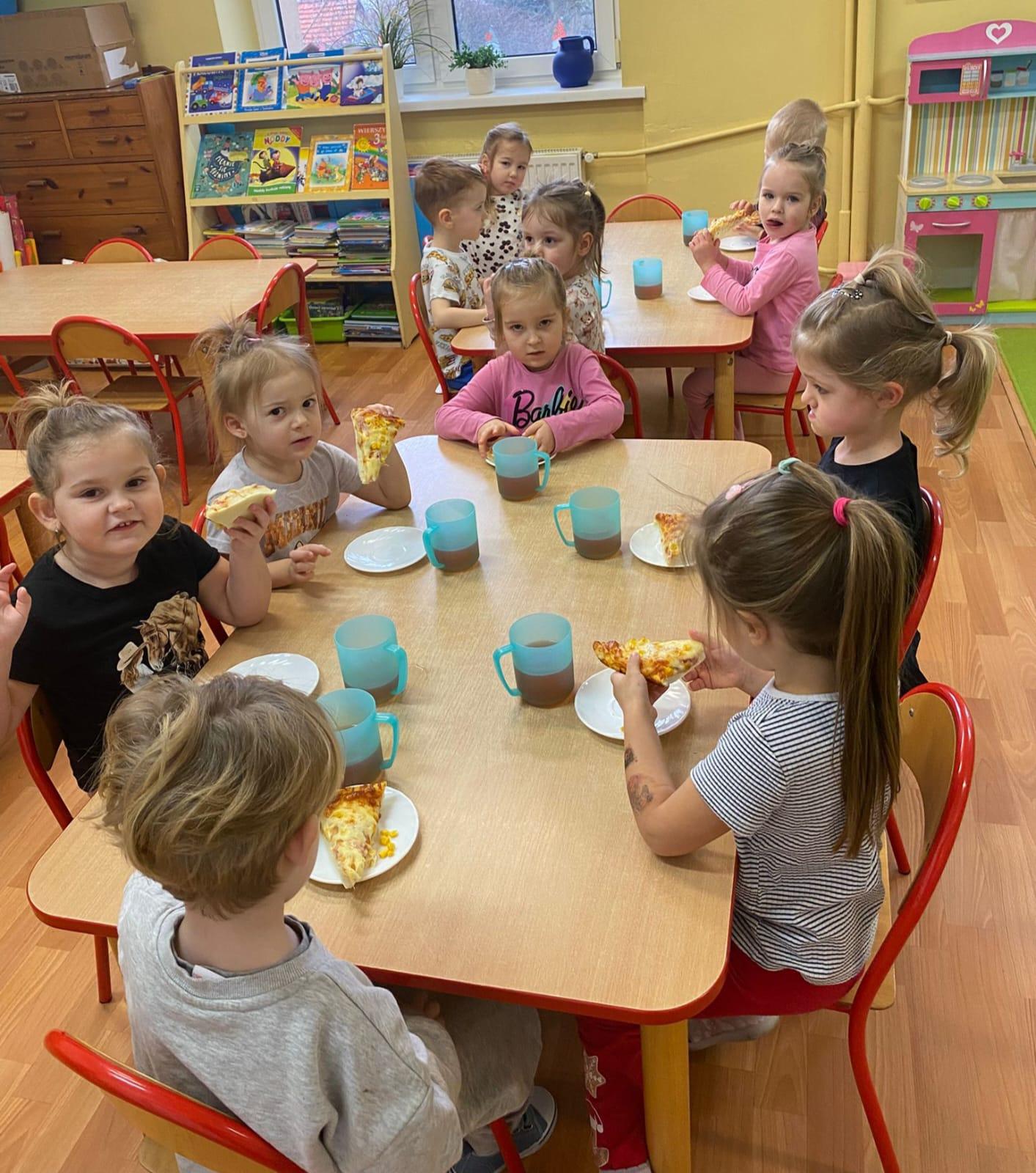 Dzieci siedzące przy stolikach i jedzące pizzę