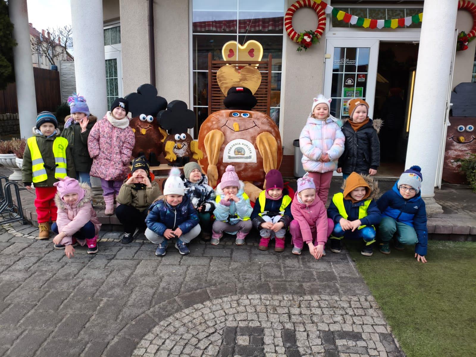 Grupa dzieci przed piekarnią z figurą dużego pączka