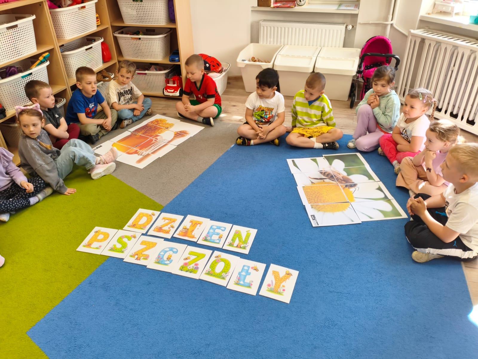 Dzieci siedzące na dywanie z dużymi zdjęciami związanymi z pszczołami
